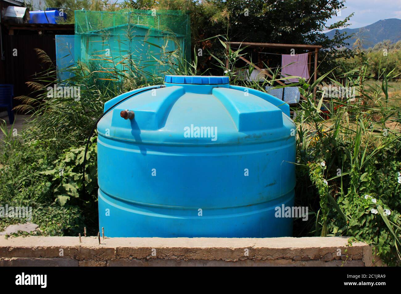 Blauer großer Kunststoff-Wassertank in der Nähe von Haus in einer trockenen Region. Die Siedlung auf dem Territorium der Republik Krim Stockfoto