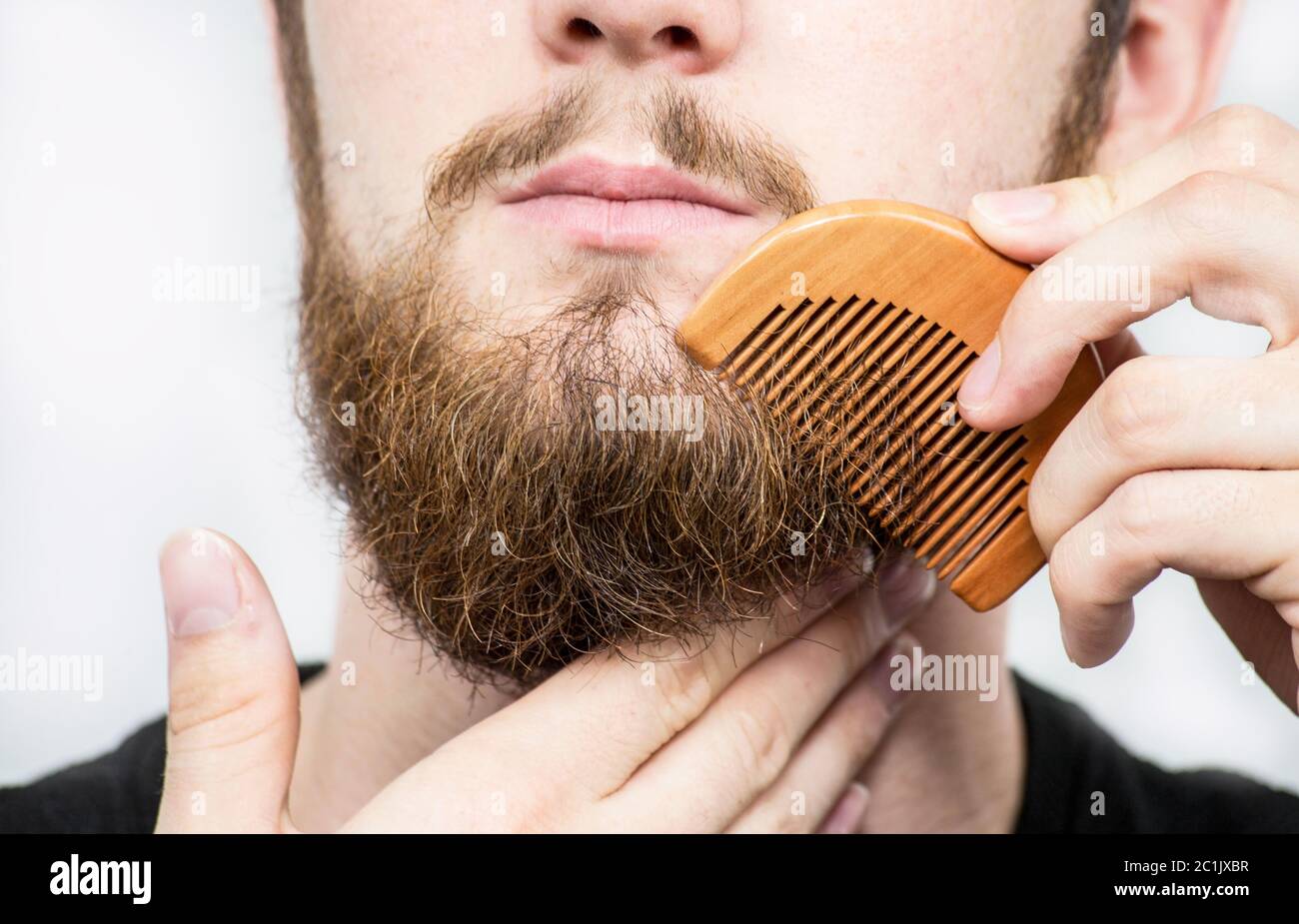 Nahaufnahme eines jungen Mannes styling seinem langen Bart mit einem Kamm, während allein in einem Studio vor einem weißen Hintergrund Stockfoto