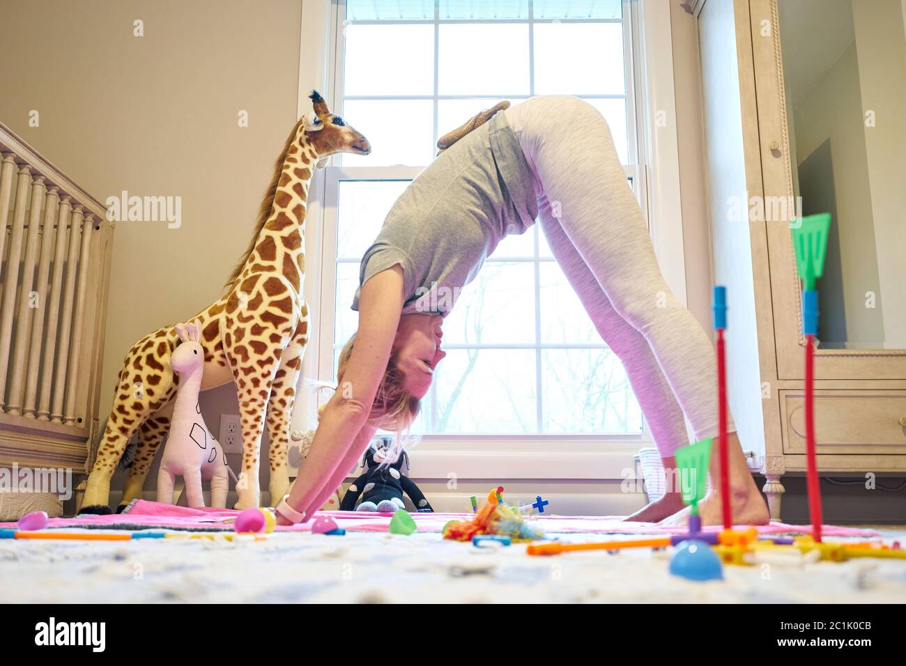 Junge Mutter in nach unten Hund Yoga-Position im Zimmer der Tochter Stockfoto