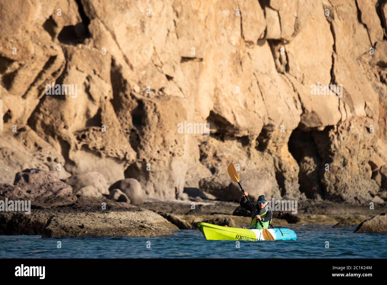 Eine Frau paddelt auf einem Platz auf dem Kajak nahe an einem Ufer mit hohen Felswänden auf Carmen Island in Loreto, Baja California, Mexiko. Stockfoto