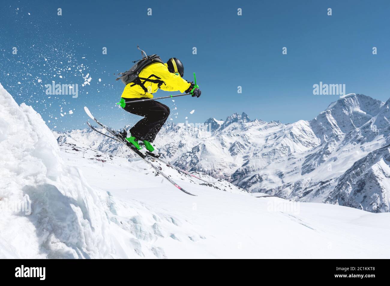Ein Skifahrer in voller Sportausrüstung springt in den Abgrund von der Spitze des Gletschers vor dem Hintergrund des blauen Himmels und Stockfoto