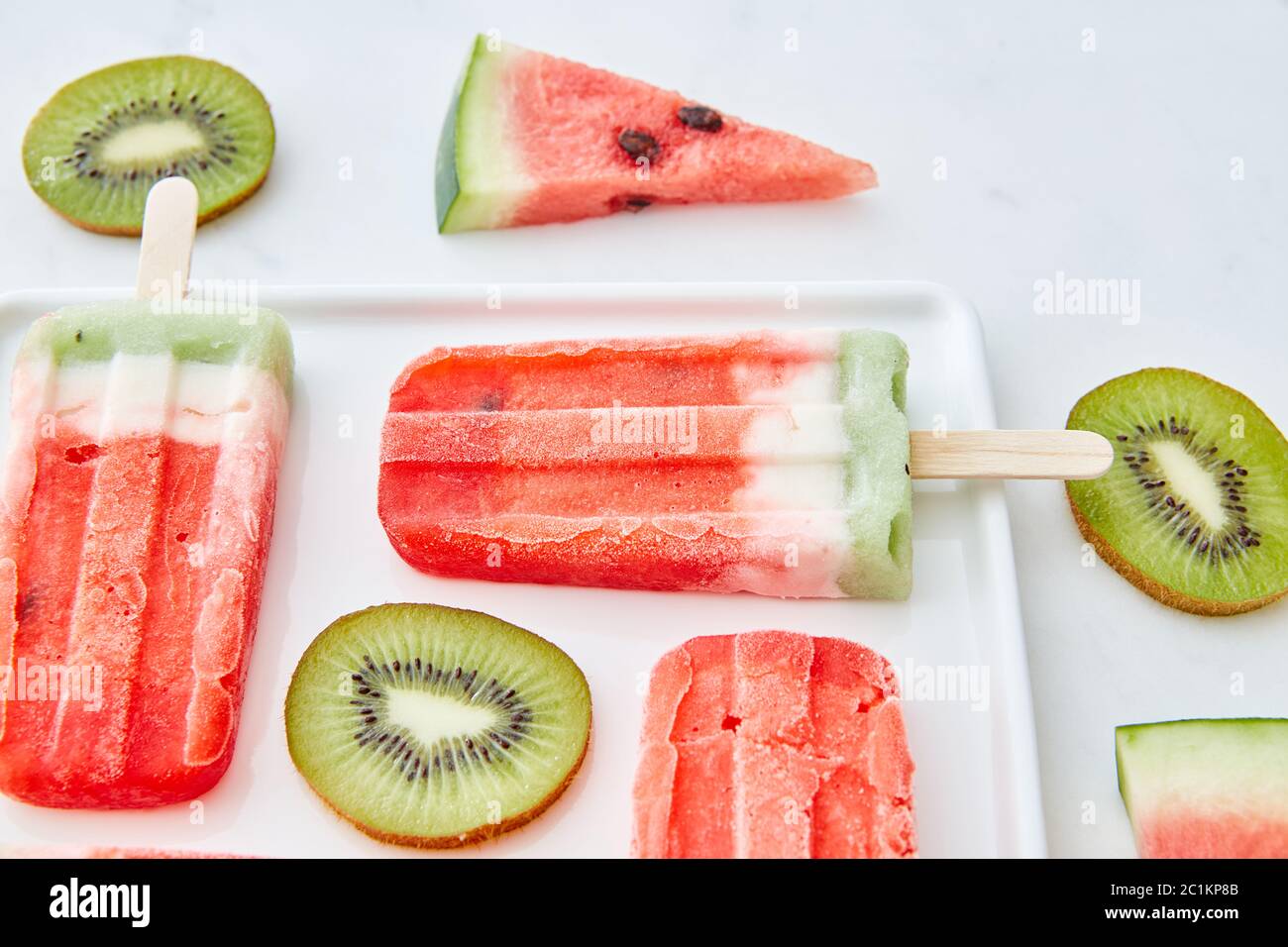 Wassermelone Eis auf einem Stock mit Stücken von Kiwi und saftigen Stücke von Wassermelone in einem Teller auf einem grauen Marmor backgro präsentiert Stockfoto