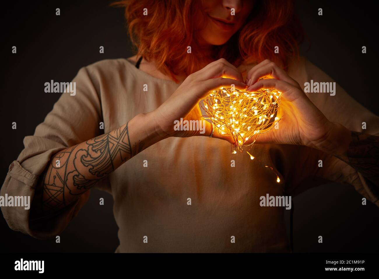 Junge Frau mit hellen Girlanden in Form von Herz auf einem dunklen Hintergrund. Stockfoto