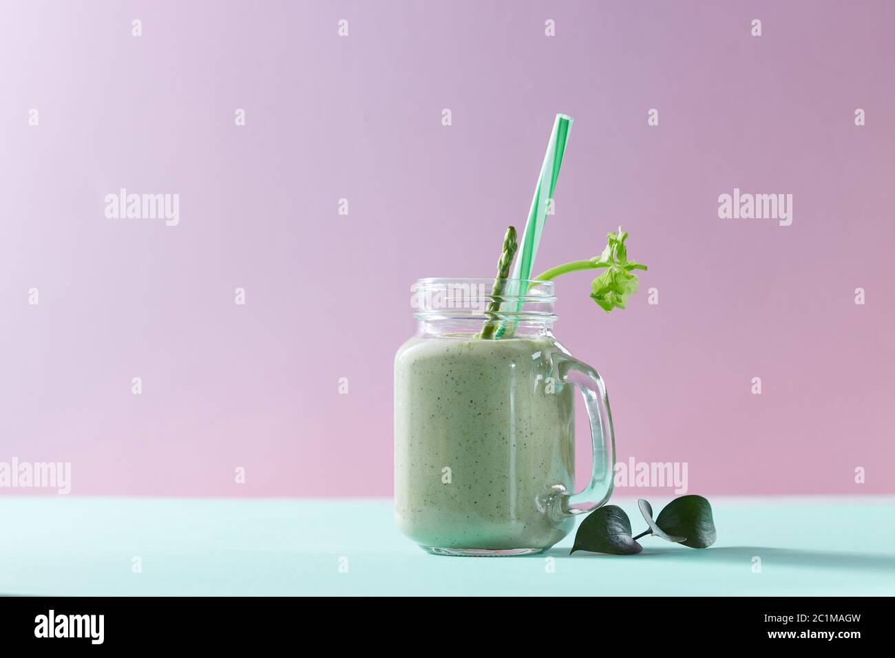 Grüner Smoothie aus grünem Bio-Gemüse mit Spargel und Sellerie in einer Glasschüssel auf duotone rosa grünem Papier Hintergrund. Stockfoto
