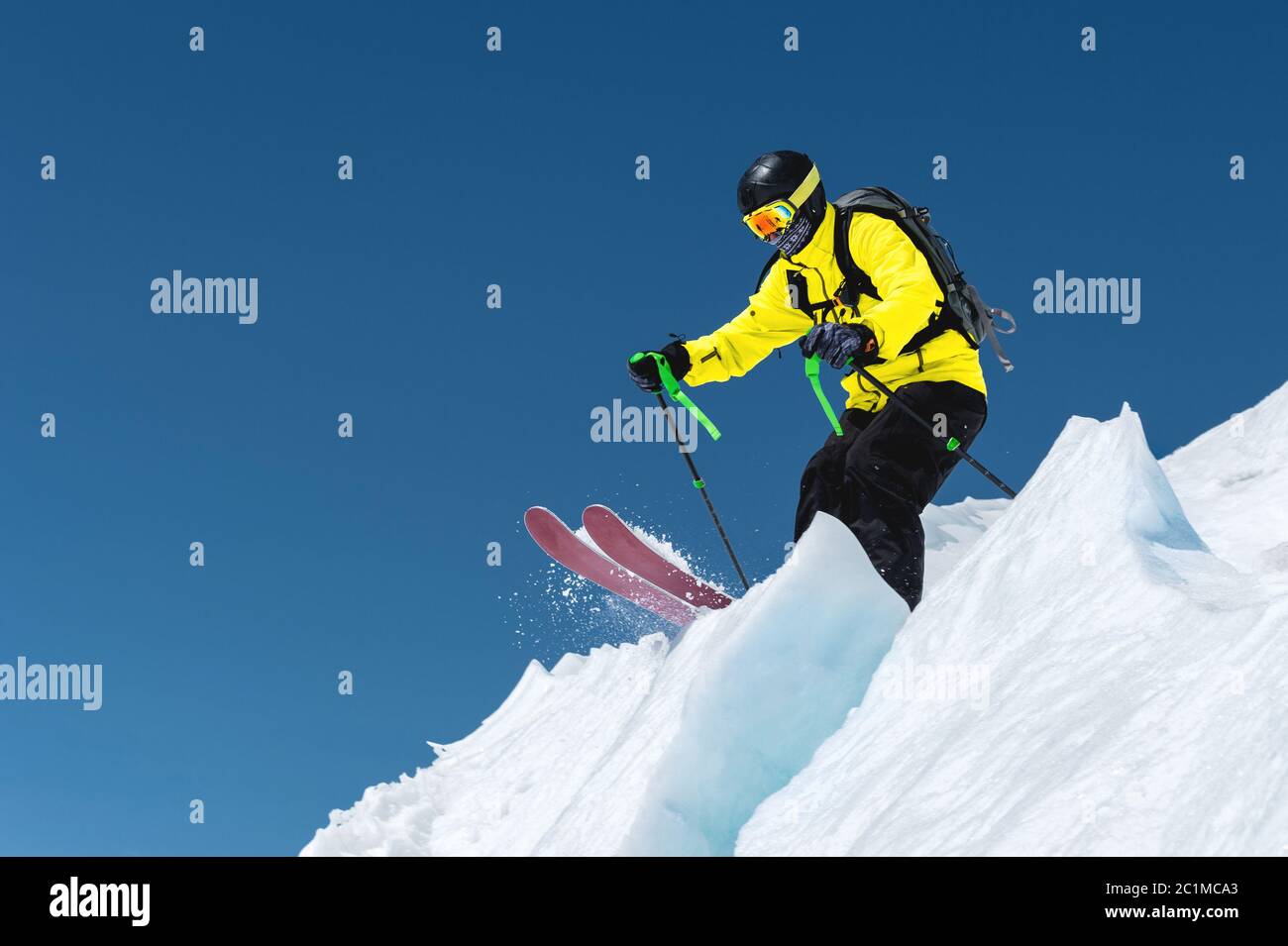 Ein Skifahrer in voller Sportausrüstung springt in den Abgrund von der Spitze des Gletschers vor dem Hintergrund des blauen Himmels und Stockfoto