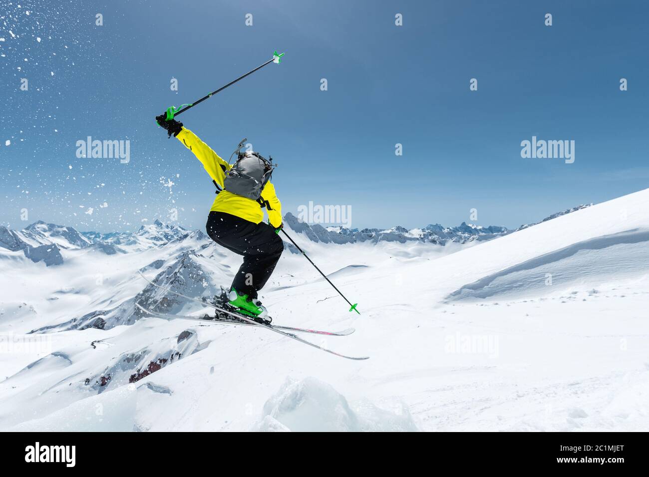 Ein Skifahrer in voller Sportausrüstung springt in den Abgrund von der Spitze des Gletschers vor dem Hintergrund des blauen Himmels und der Stockfoto