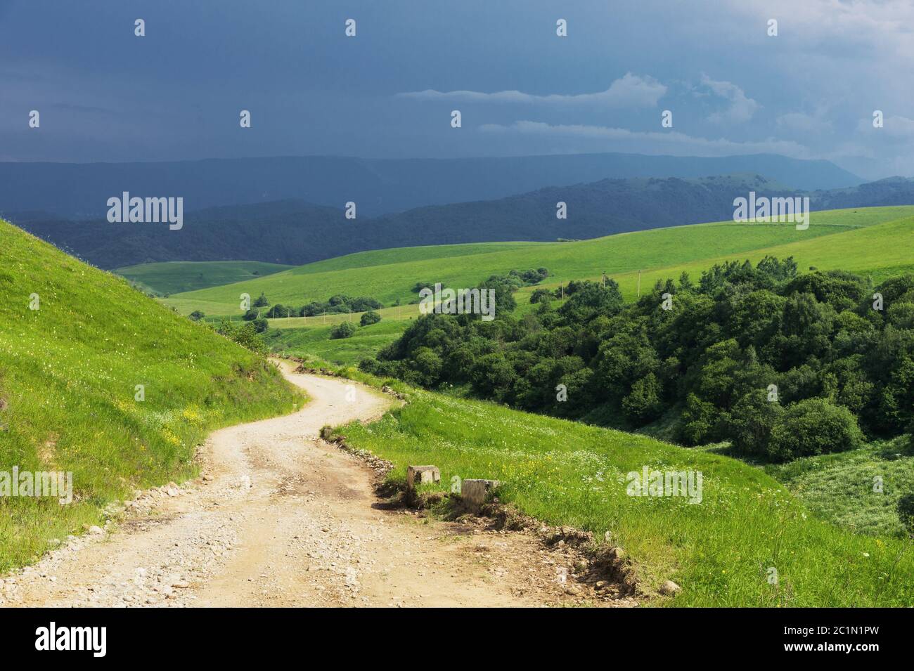 Eine Landstraße zwischen den Hügeln mit Bäumen an den Rändern und Gewitterwolken im Sommer Stockfoto