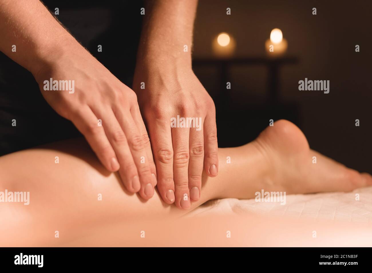 Nahaufnahme der männlichen Hände, die in einem dunklen Raum mit Kerzen im Hintergrund eine Kalbsmassage der weiblichen Beine machen. Kosmetologie und Spa Trea Stockfoto