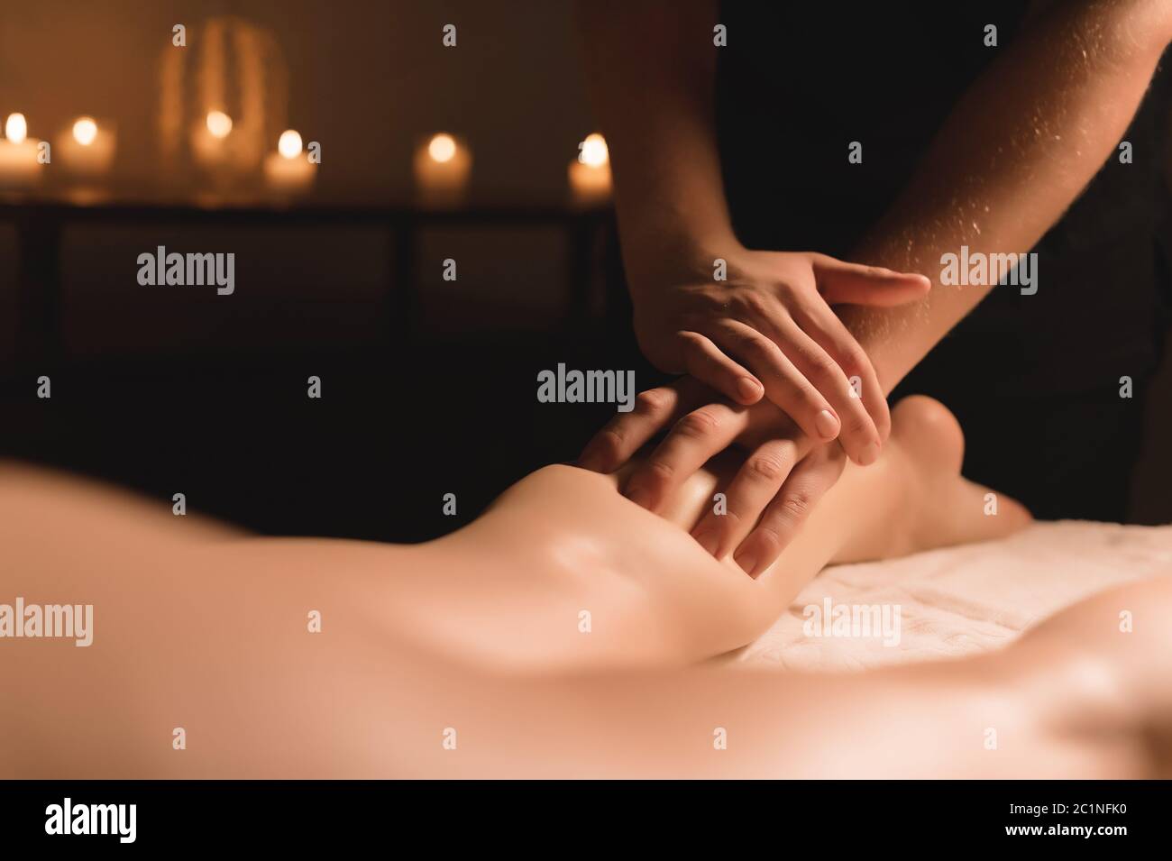 Nahaufnahme der männlichen Hände, die in einem dunklen Raum mit Kerzen im Hintergrund eine Kalbsmassage der weiblichen Beine machen. Kosmetologie und Spa Trea Stockfoto