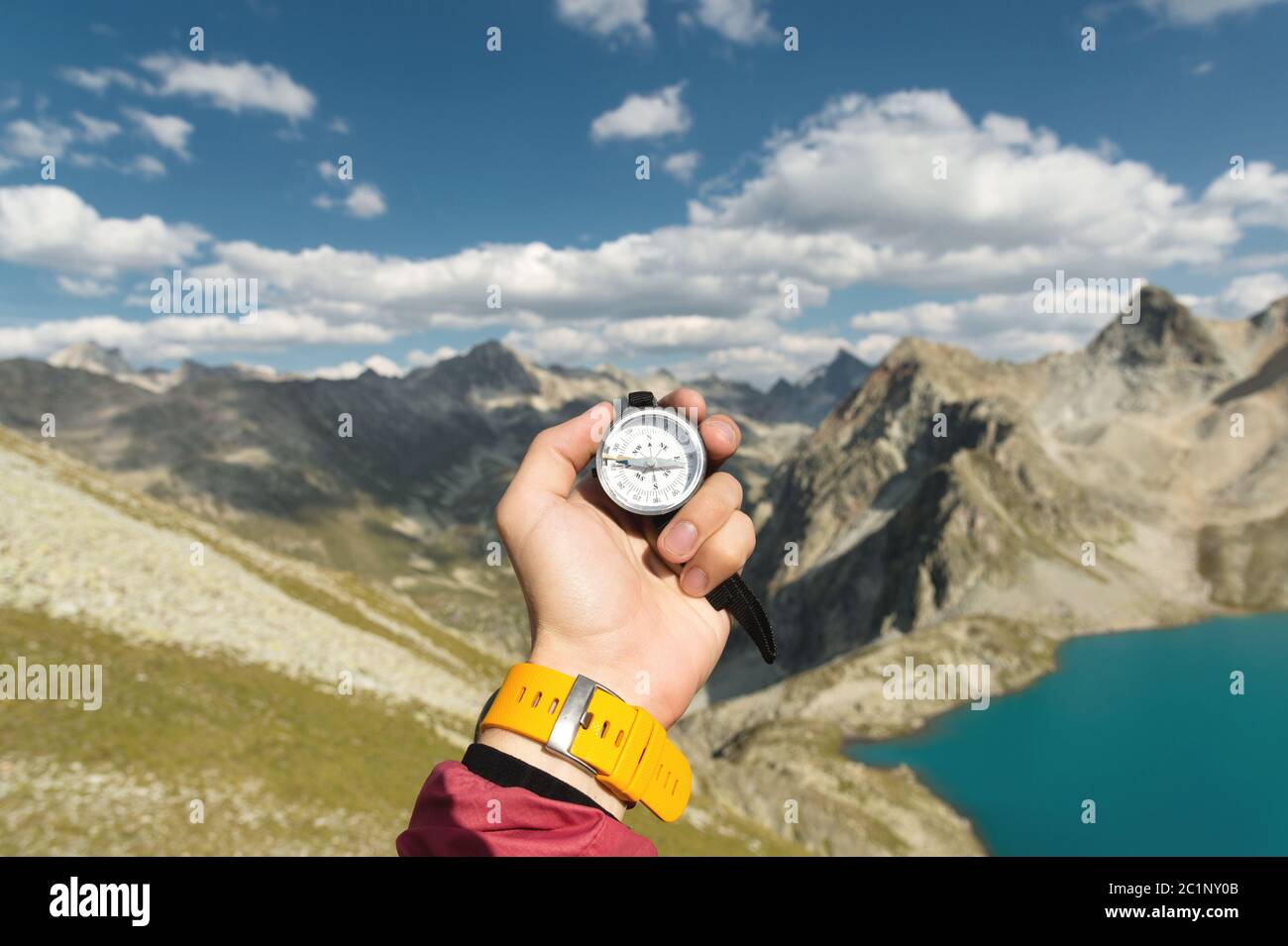 Eine Männerhand hält einen magnetischen Taschenkompass für die Navigation vor der Kulisse eines felsigen Abhangs und eines Bergsees. Die Conce Stockfoto