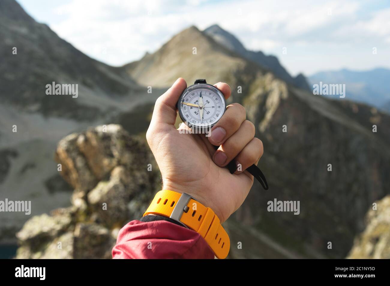 Eine Männerhand hält einen magnetischen Taschenkompass für die Navigation vor der Kulisse eines felsigen Abhangs und eines Berges. Das Konzept von Stockfoto