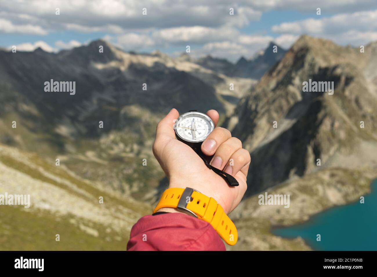Eine Männerhand hält einen magnetischen Taschenkompass für die Navigation vor der Kulisse eines felsigen Abhangs und eines Bergsees. Die Conce Stockfoto