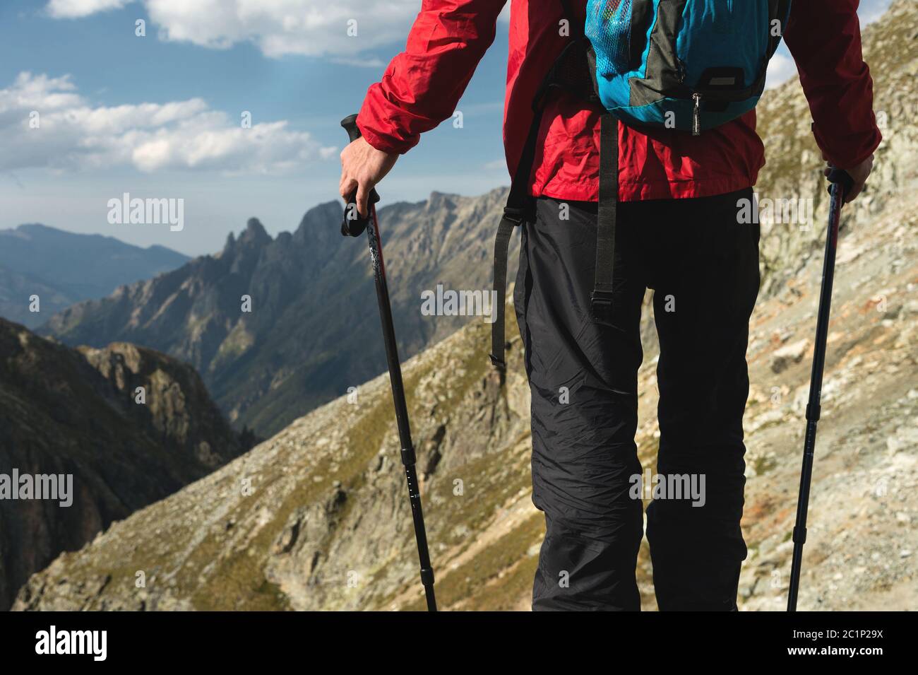Der Körper des Menschen mit einem Rucksack und Trekking-Stöcke steht auf einem Felsen vor dem Hintergrund felsigen Tal hoch in der Halterung Stockfoto