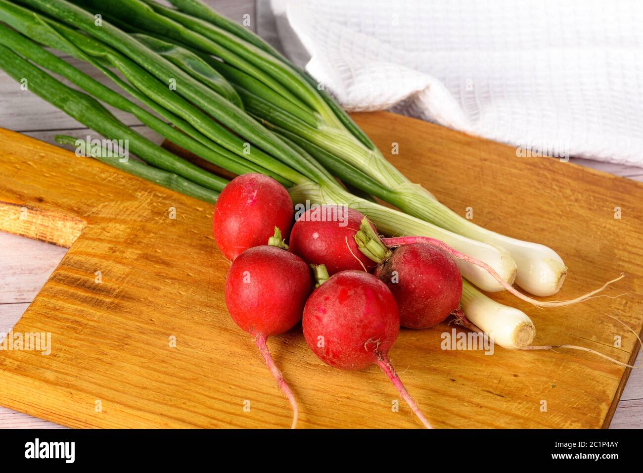 Grüne Zwiebeln und Radieschen auf dem Tisch auf dem Brett Nahaufnahme Stockfoto