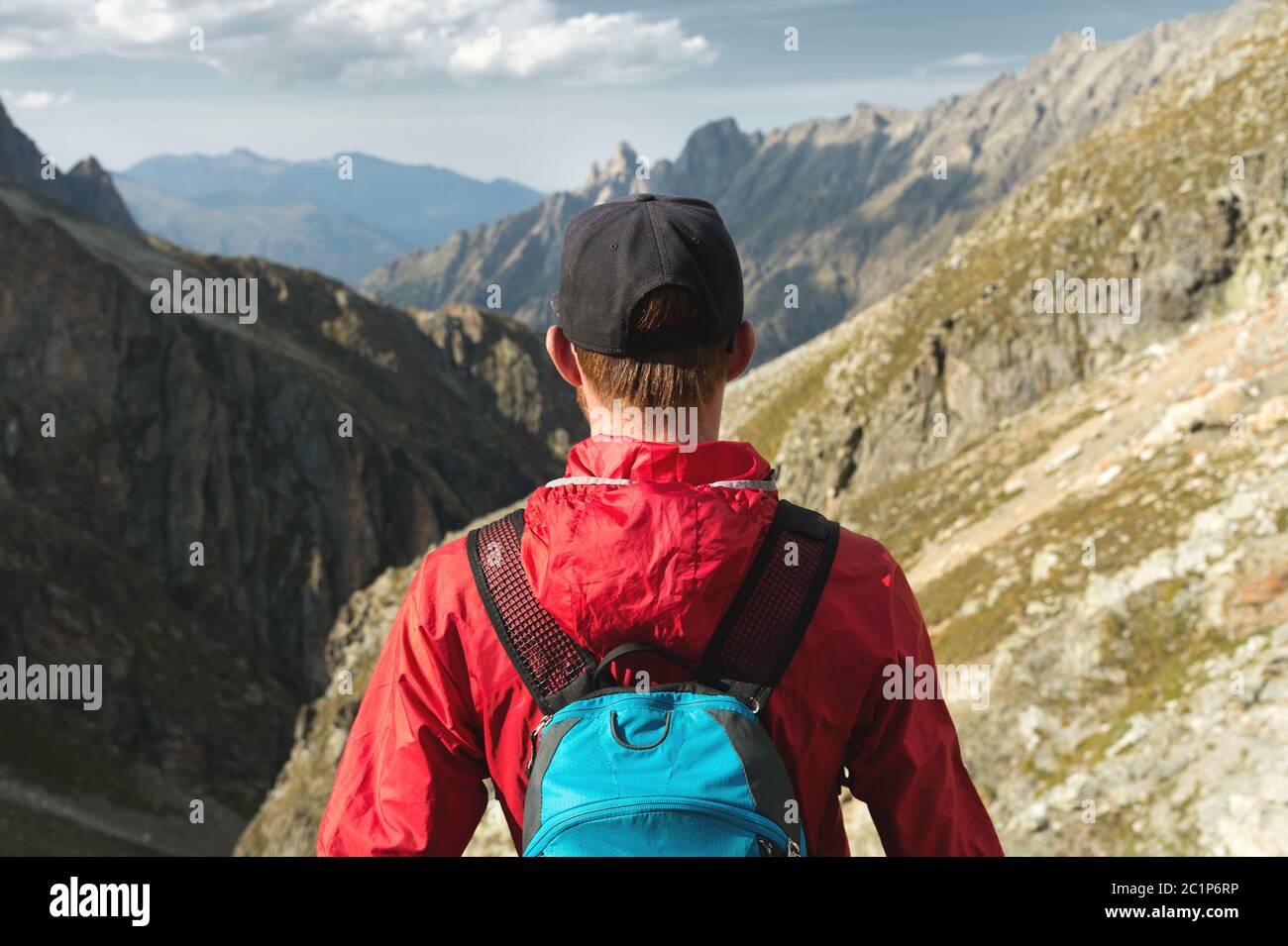 Ein bärtiger Mann in einer Mütze mit Rucksack steht auf einem Felsen und blickt in ein felsiges Tal hoch in den Bergen. Das Konzept Stockfoto