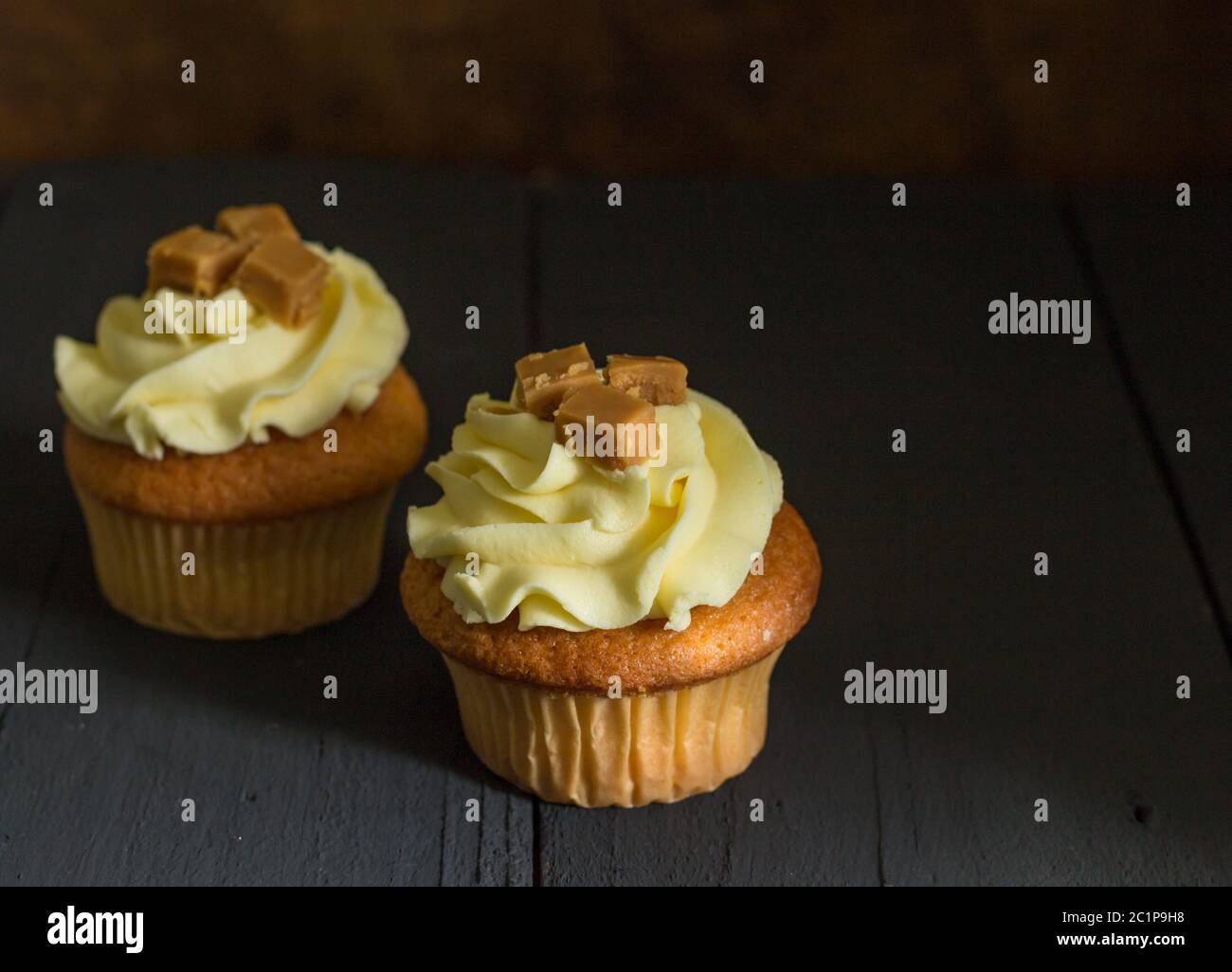 Zwei butterscotch Caramel fudge Cup Cakes auf rustikalen Schwarzer Tisch mit selektiven Fokus eingerichtet Stockfoto