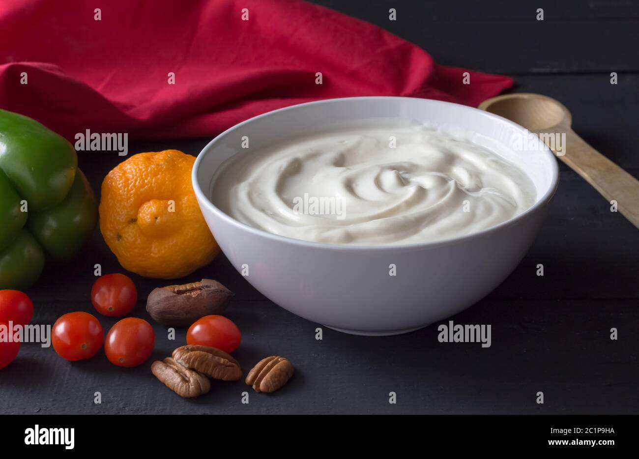 Joghurt in einer Schüssel - natürliches griechisches Joghurt Stillleben mit Gemüse und Nüssen auf schwarzem Hintergrund Stockfoto