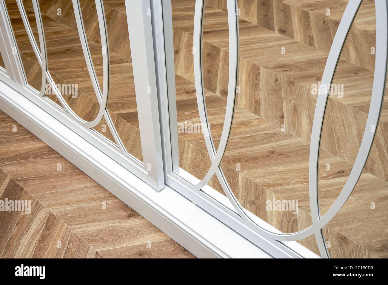 Schranktüren mit Spiegelschiebespiegel und Überzügen. Weißer Schiebespiegel Kleiderschrank auf Parkett Hintergrund. Nahaufnahme Stockfoto