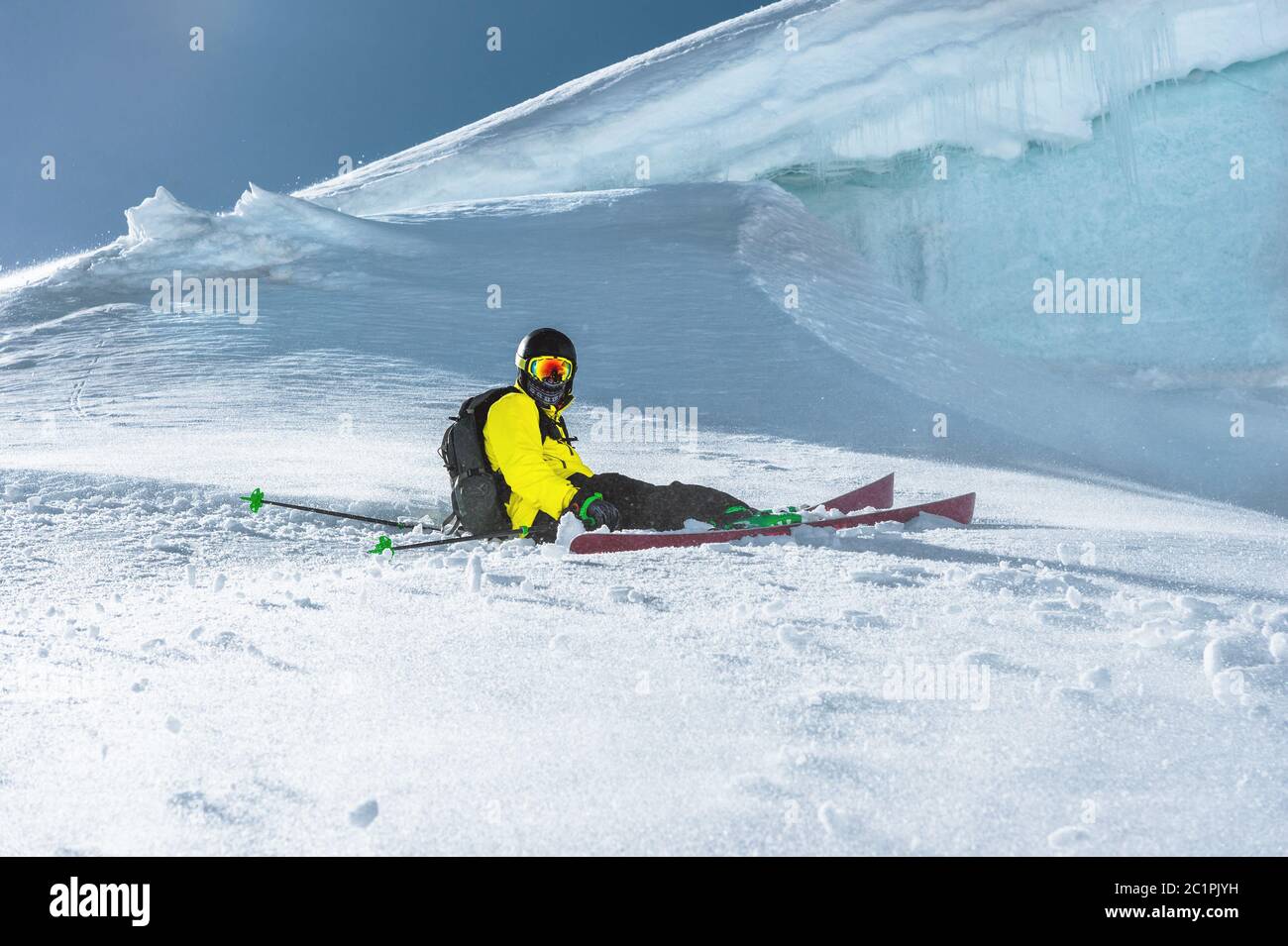 Der Sportler sitzt auf einem verschneiten Hang vor dem Hintergrund der Eiswand. Professionelles Skifahren. Winterurlaub in der Moun Stockfoto