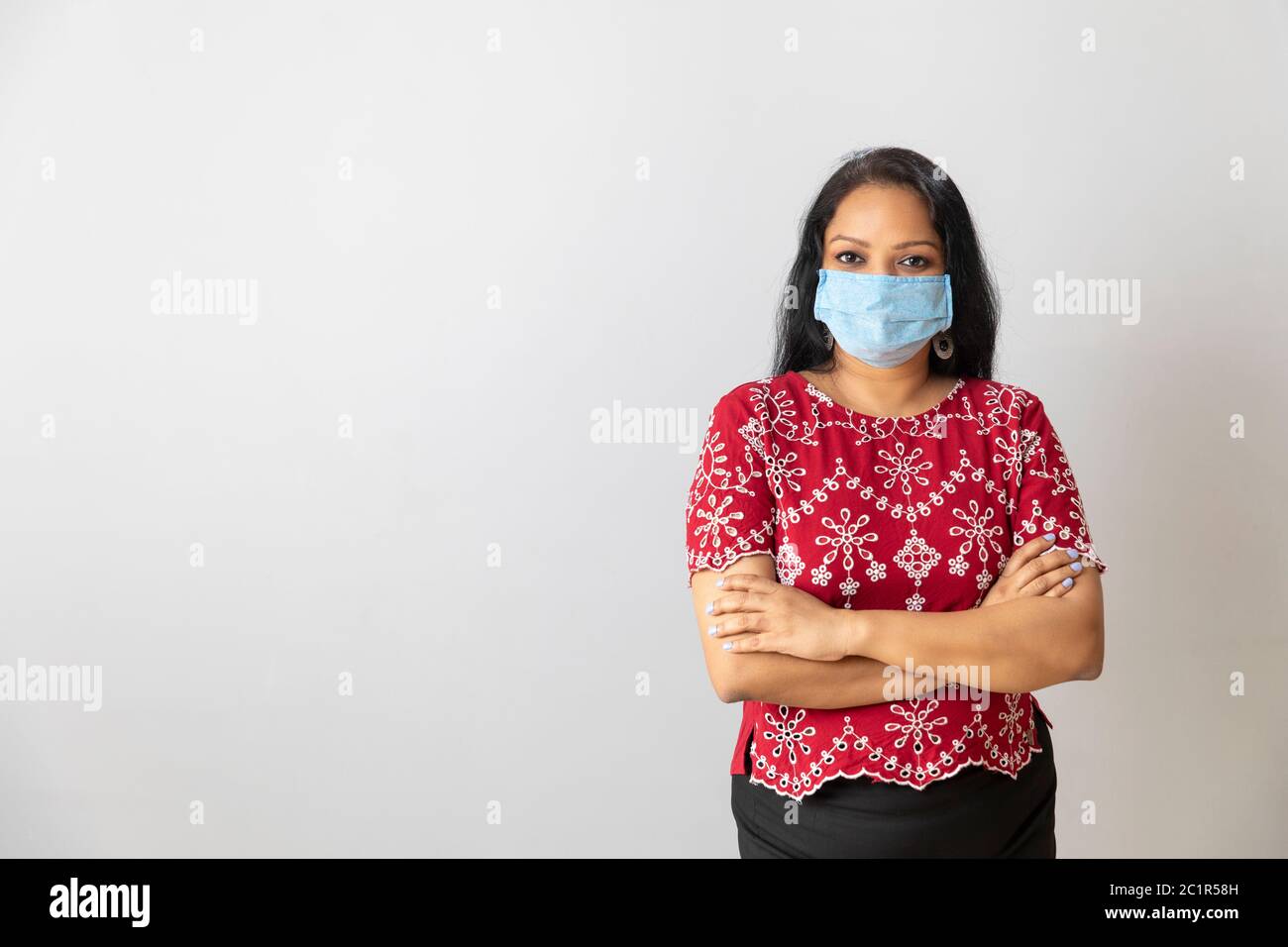 Eine indische Dame in einem roten Kleid trägt eine Maske Stockfoto