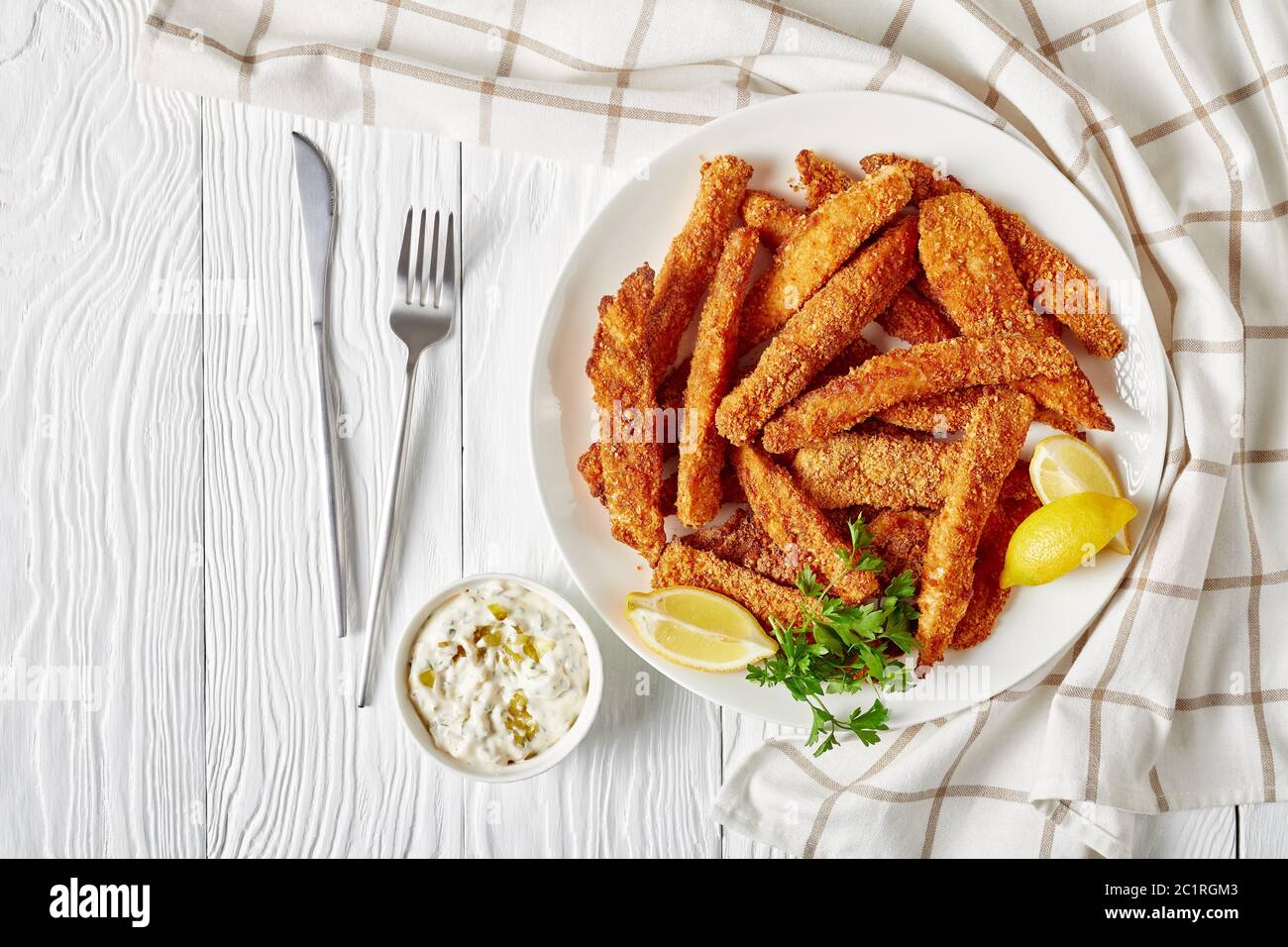 Fischstäbchen, Fischfiletfinger paniert und frittiert auf einem weißen Teller auf einem Holztisch mit Tartarsauce und Zitronenkeilchen serviert, horizontale Ansicht Stockfoto