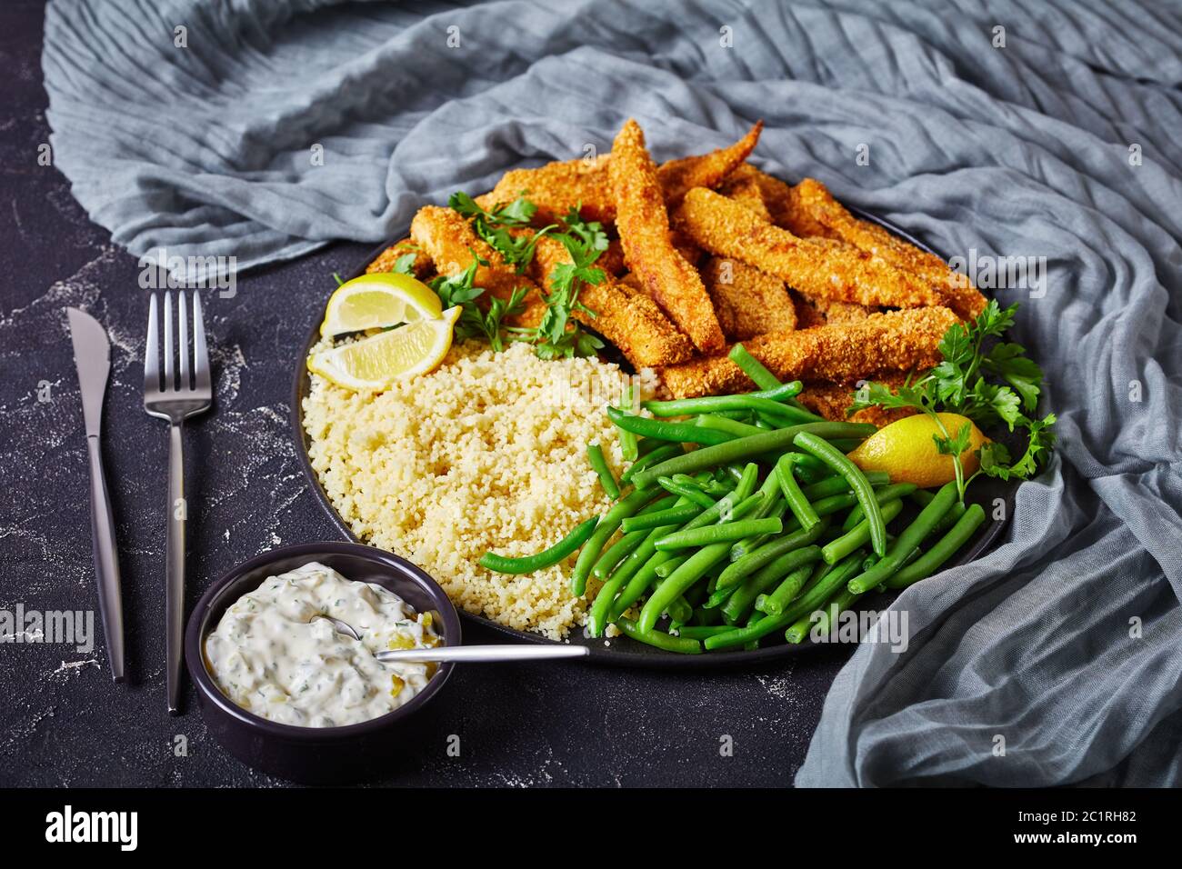 Fischstäbchen, Fischfiletfinger paniert und frittiert auf einem schwarzen Teller mit Couscous und gedämpften grünen Bohnen auf einem Betontisch mit Tartar serviert Stockfoto