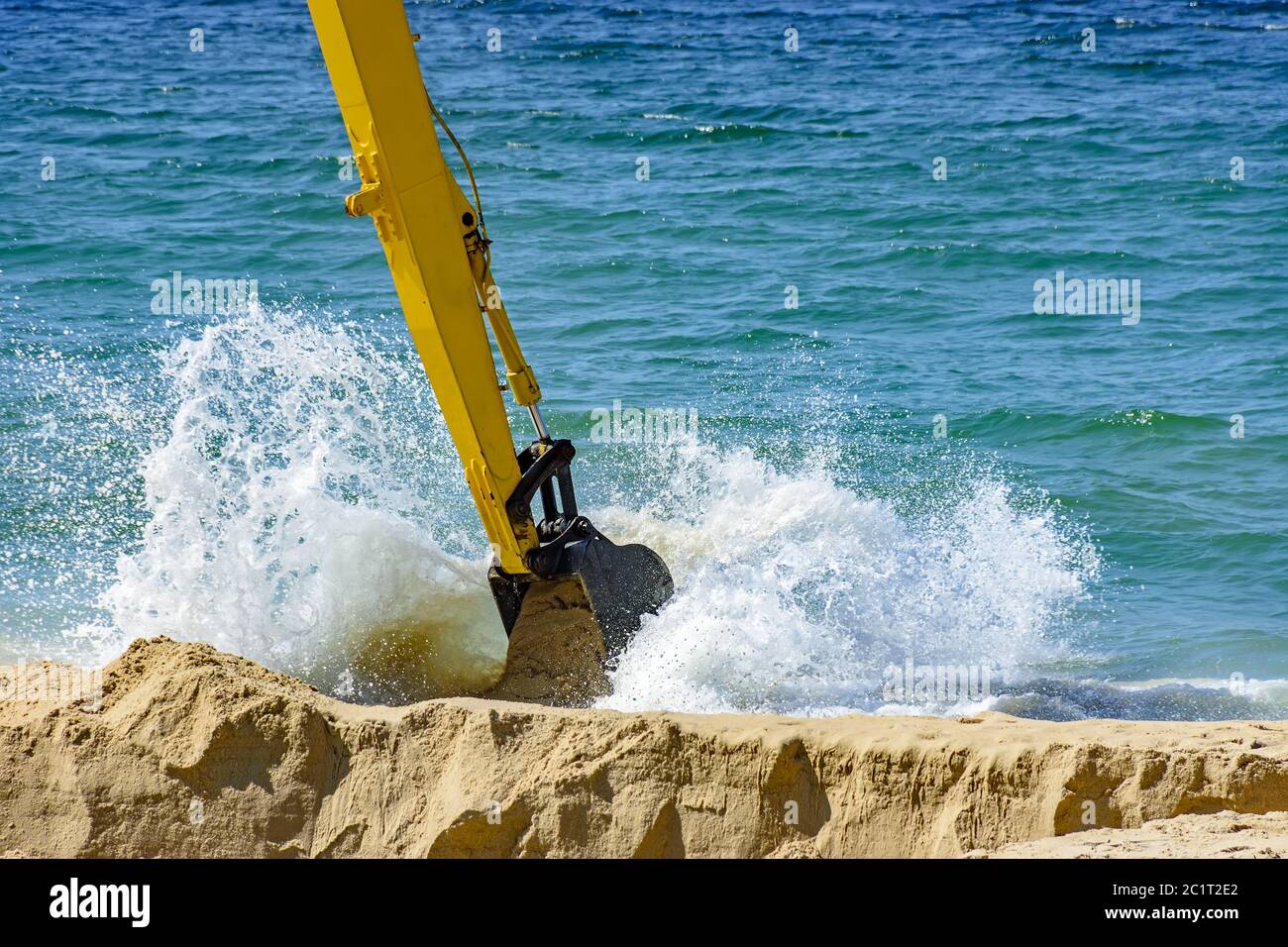 Bagger entfernen Sand vom Strand und spielen im Meer mit Wasser Spray Stockfoto