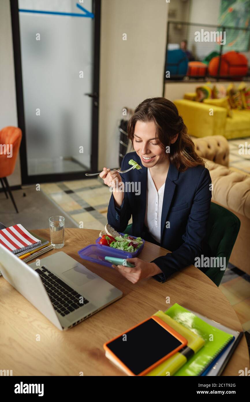 Essen Mädchen mit einem Smartphone im Büro Stockfoto