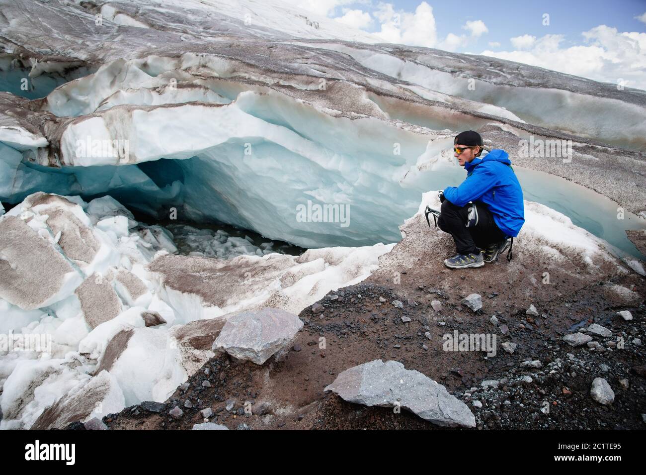 Reisende in Mütze und Sonnenbrille sitzt in den verschneiten Bergen auf dem Gletscher. Reisende in einer natürlichen Umgebung Stockfoto