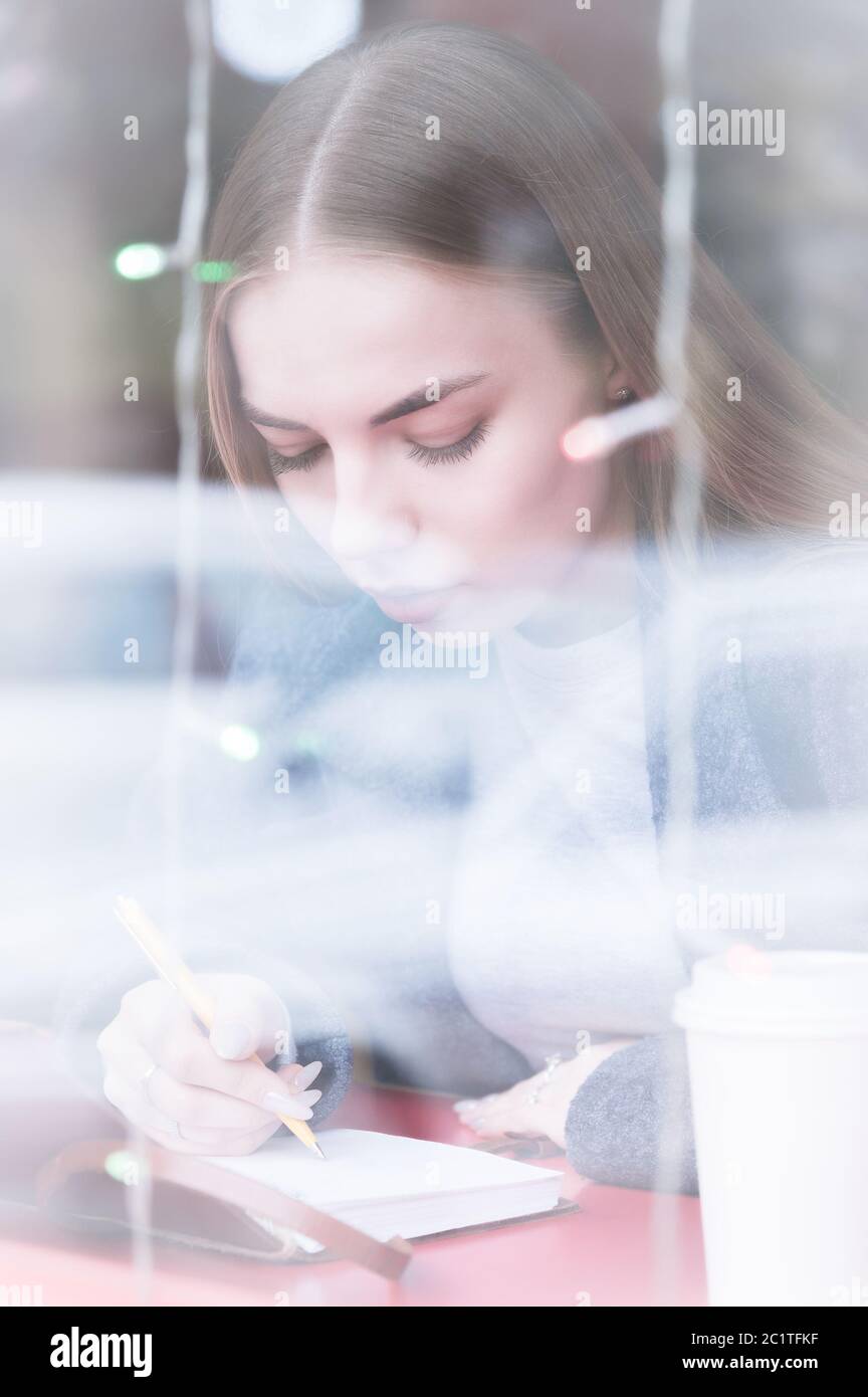 Porträt eines attraktiven jungen Journalistin Mädchen mit Stift und Notizblock im Café hinter der Vitrine. Kontrastfreie Sicht durch Wind Stockfoto