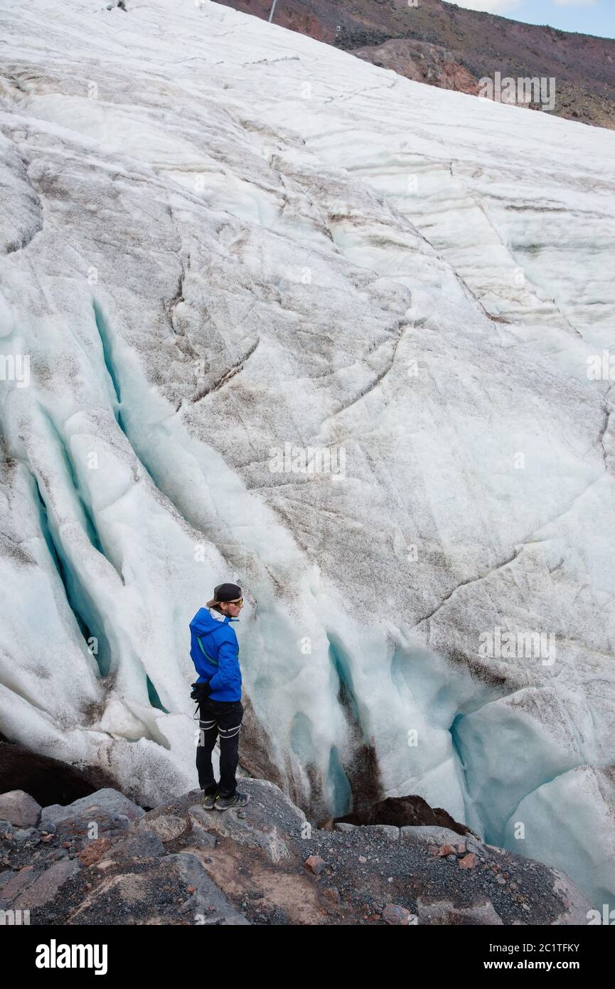 Reisende in Mütze und Sonnenbrille steht in den verschneiten Bergen auf dem Gletscher. Reisende in einer natürlichen Umgebung Stockfoto