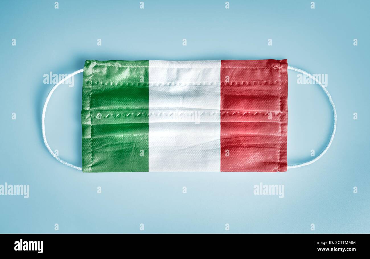 Covid-19 Coronavirus Schutzkonzept: Medizinische Einweg-Gesichtsmaske mit Italien Flagge auf blauem Hintergrund. Stockfoto