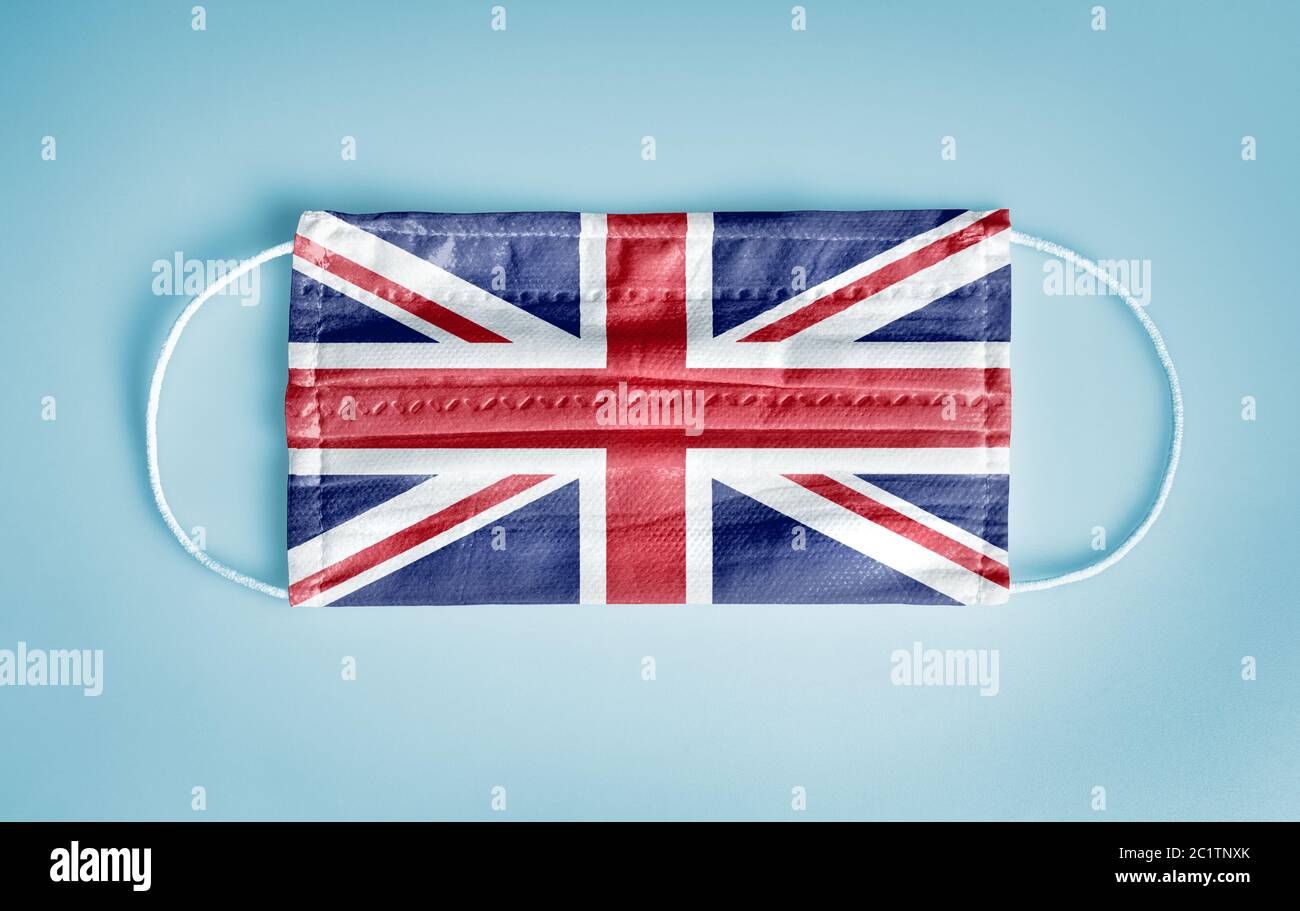 Covid-19 Coronavirus Schutzkonzept: Medizinische Einweg-Gesichtsmaske mit Großbritannien Flagge auf blauem Hintergrund. Konzept der sozialen Distanzierung. Stockfoto