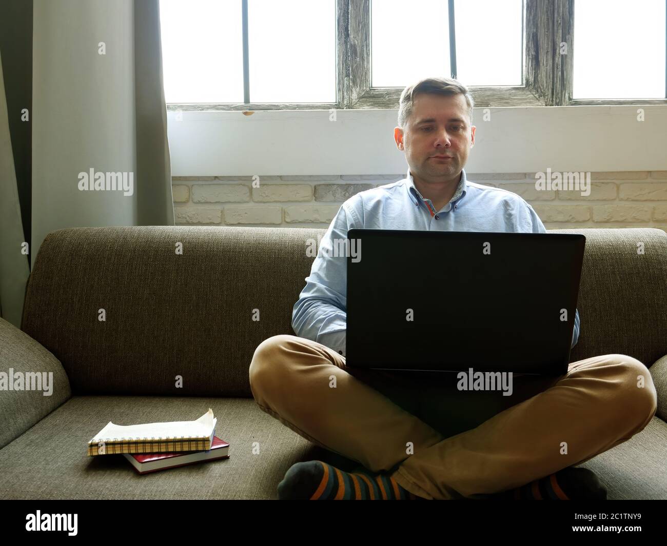 Mann mit Laptop arbeitet zu Hause. Quarantänekonzept. Freelancer sitzt auf dem Sofa und gibt auf der Tastatur ein. Stockfoto