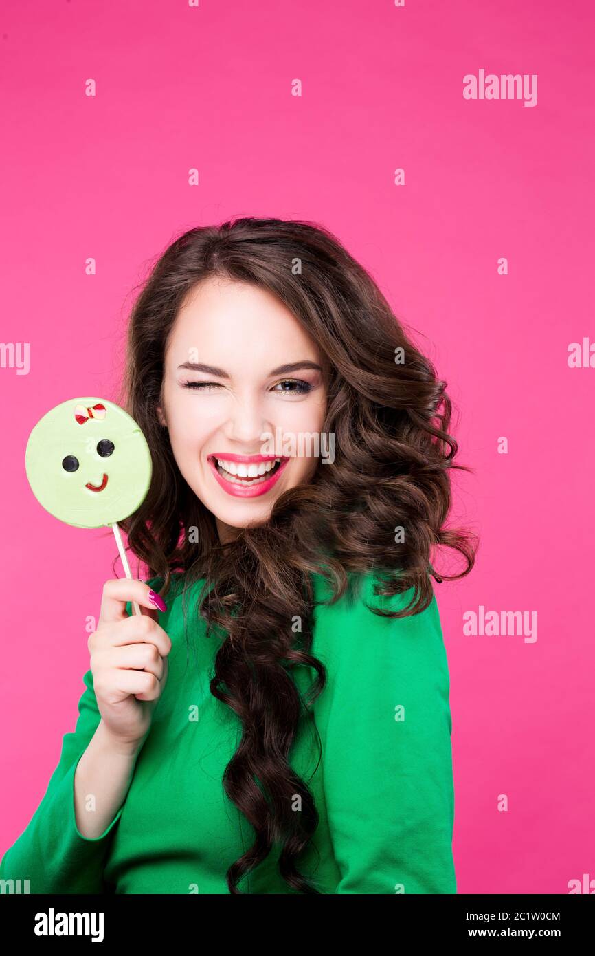 Fröhliche hübsche Frau mit einem Candy zwinkert lacht zeigt Sprache. Brunette Mädchen modisch und stilvoll auf rosa Hintergrund in S Stockfoto