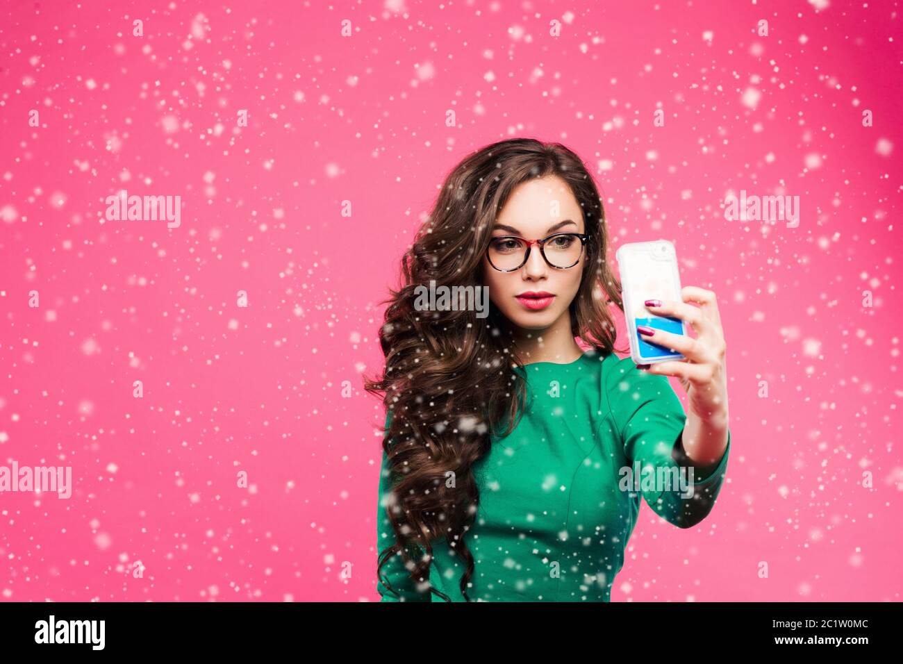 Hübsche Brünette Mädchen mit langen welligen Haaren zeigt Stick out und selbst Porträt auf ihrem Smartphone. Tragen grüne Jacke und Stockfoto