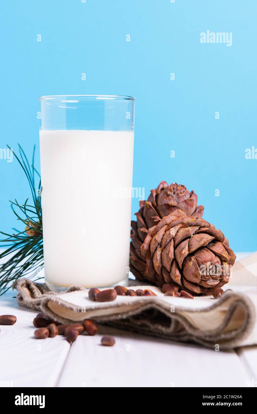 Laktosefreies Milchkonzept, Glas mit Zedernmilch, Zapfen und Nüssen auf weißem Tisch auf blauem Hintergrund Stockfoto