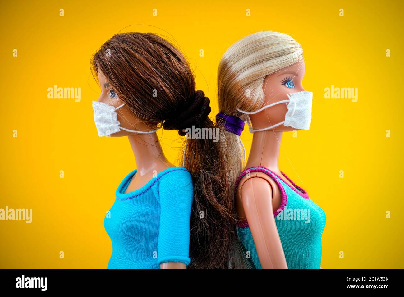 Tambow, Russische Föderation - 12. Juni 2020 zwei Barbie Puppen mit medizinischen Masken stehen zurück an den Rücken vor gelbem Hintergrund. Studioaufnahme. Stockfoto