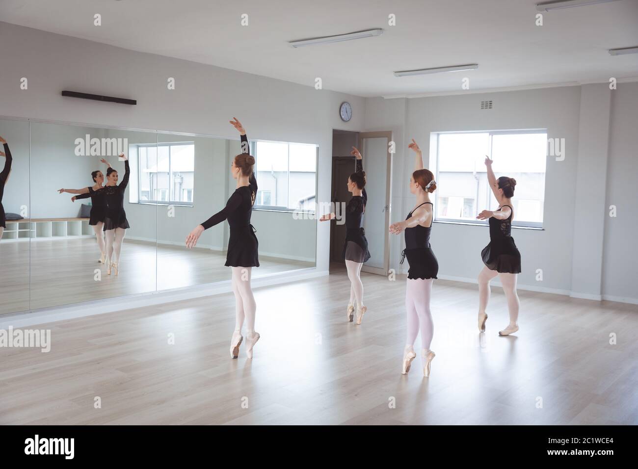 Kaukasische Balletttänzerinnen in schwarzen Anzügen üben während einer Klasse in einem hellen Studio Stockfoto