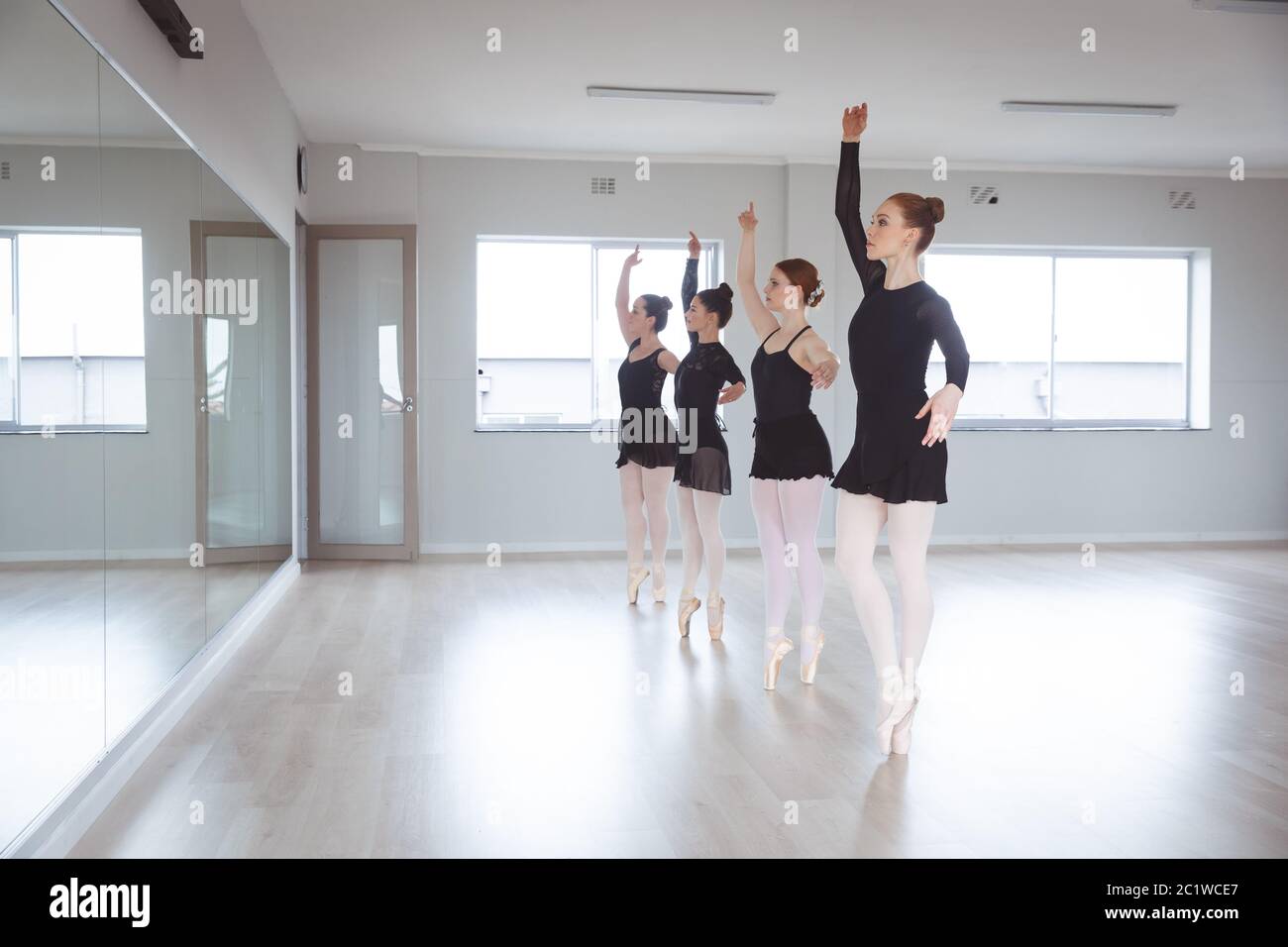 Kaukasische Balletttänzerinnen in schwarzen Anzügen üben während einer Klasse in einem hellen Studio Stockfoto