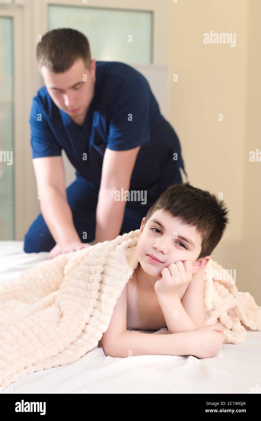 Männlicher Handtherapeut massiert Kälber eines kleinen Patienten. Kleine nachdenkliche Junge an der Rezeption des Verfahrens der Massage in Th Stockfoto