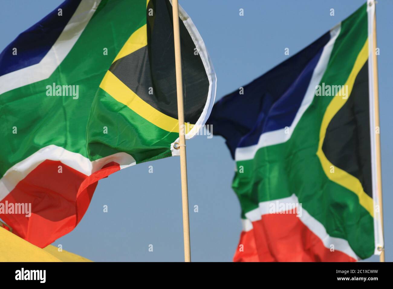 Ein paar bunte südafrikanische Flaggen wehen im Wind, während sie auf dünnen Stangen gegen den klaren wolkenlosen blauen Himmel montiert sind. London, England Stockfoto