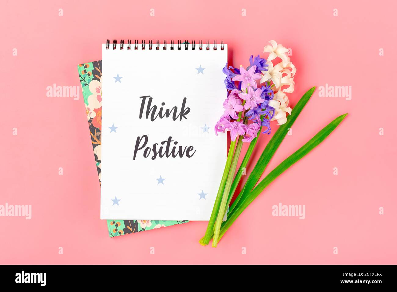 Weißes Notizbuch, Blumenstrauß von Hyazinthen auf rosa Hintergrund Flat Lay Draufsicht Text Think positive - Motivations-Slogan Kreatives Konzept Stockfoto