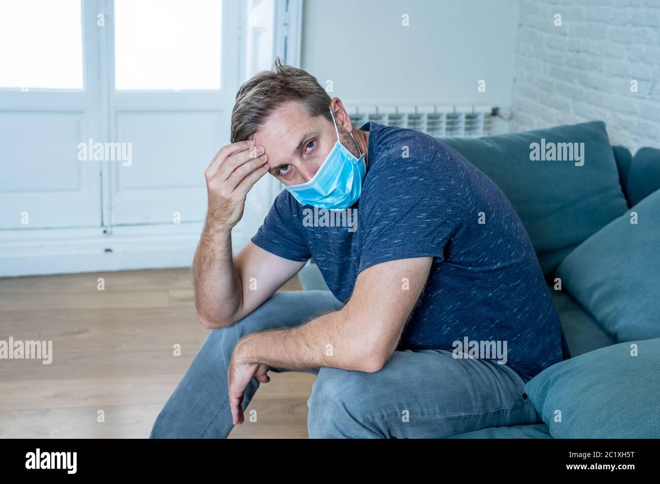 Trauriger Mann mit Schutzmaske zu Hause Wohnzimmer Couch Gefühl müde und besorgt leiden Depression inmitten Coronavirus Lockdown und soziale distan Stockfoto