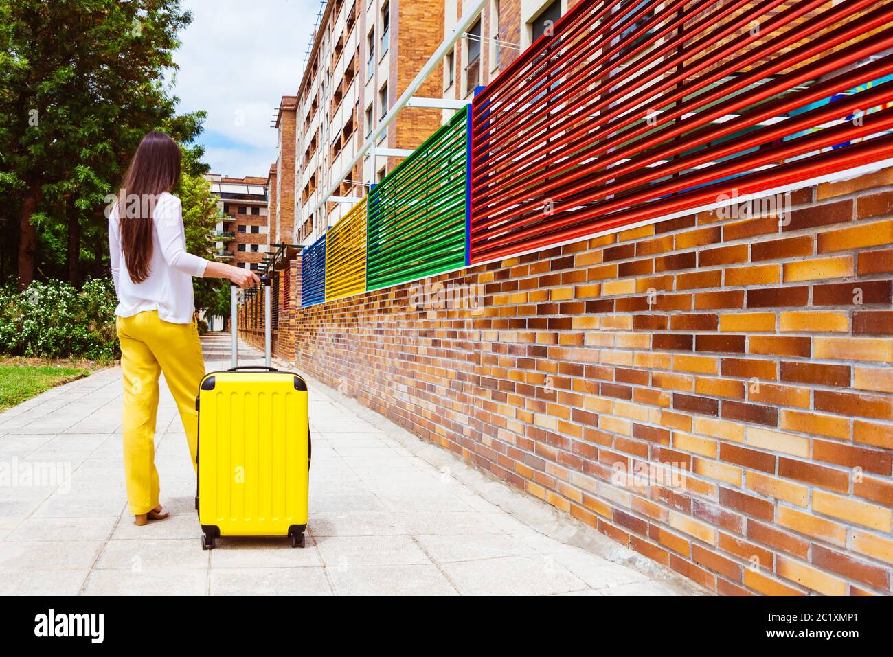 Frau auf dem Rücken mit einem gelben Koffer auf der Straße Stockfoto