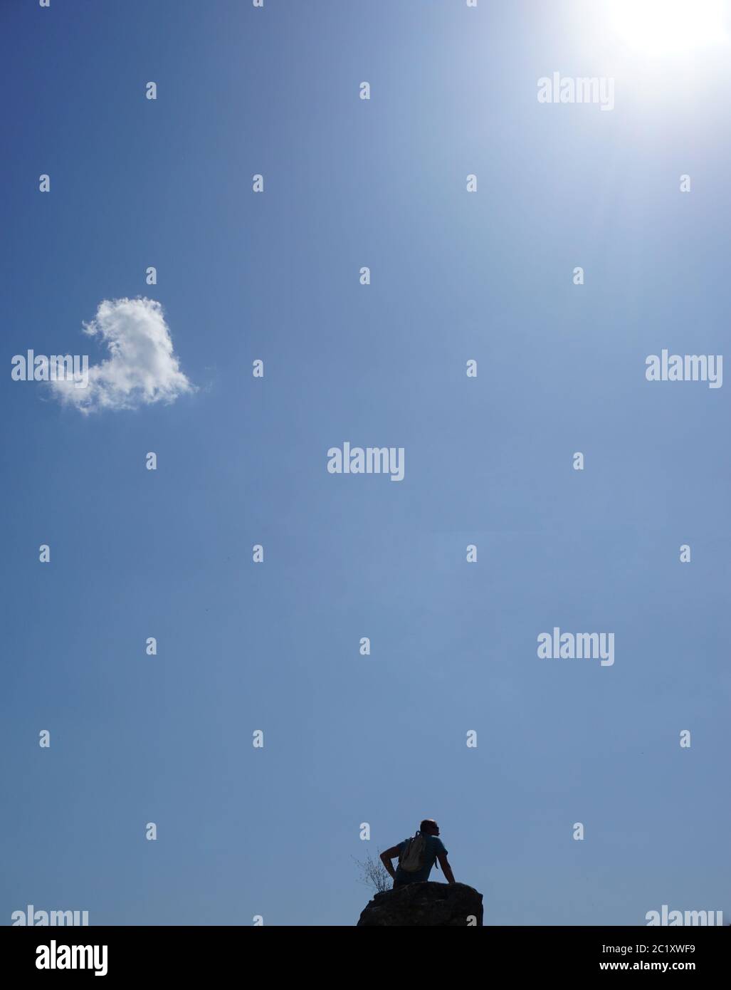 Ein Mann ruht auf einem Felsen, an einem sonnigen Sommertag. Der Himmel ist blau und hat eine herzförmige Wolke. Stockfoto