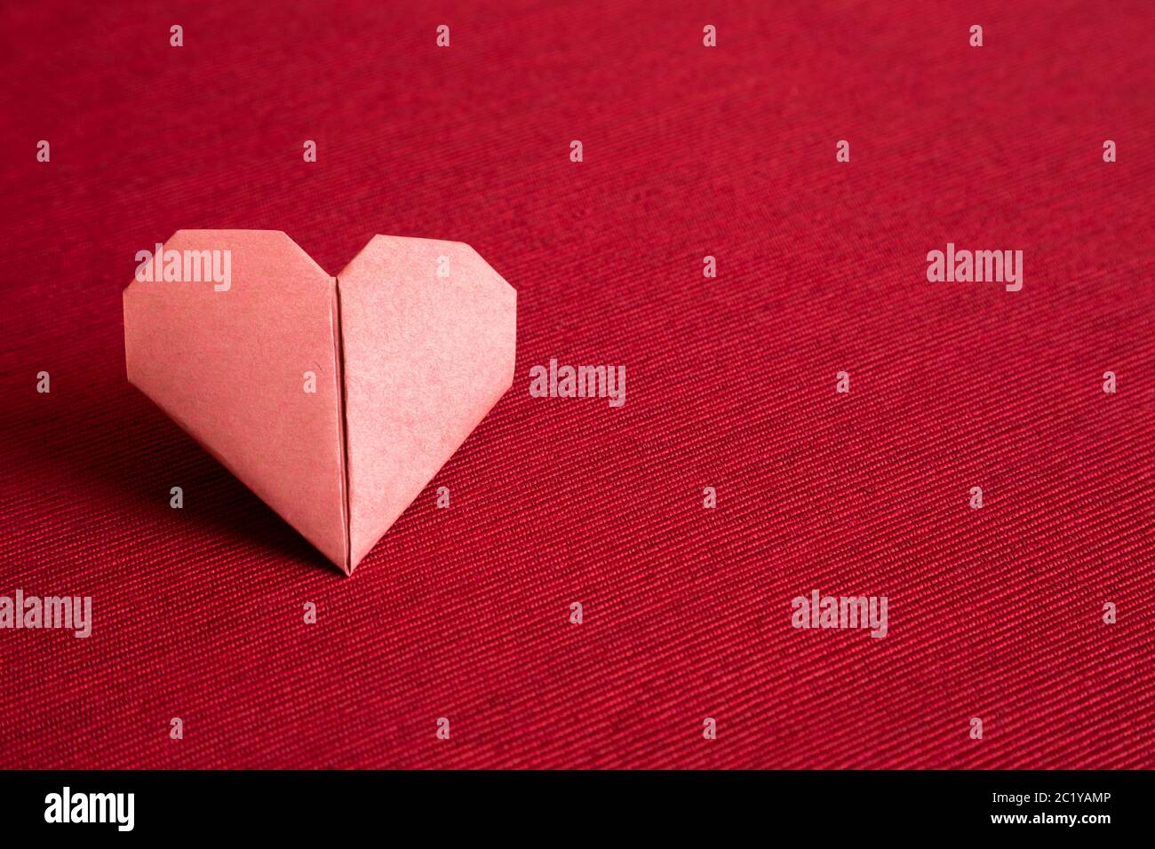 Rotes Papier Herz Origami auf rotem Stoff Hintergrund. Copy Space Stockfoto