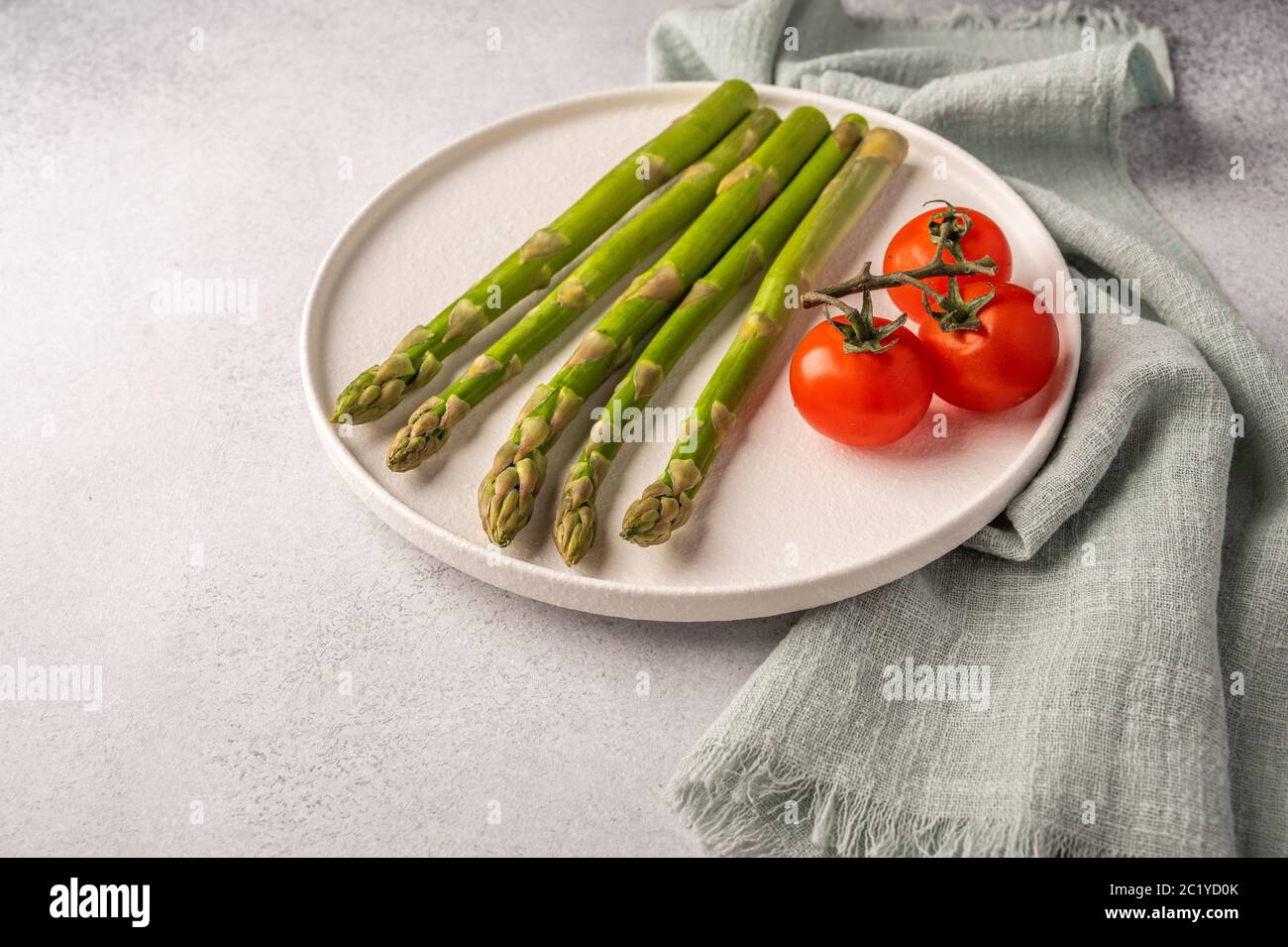 Nahaufnahme von frischem Spargel und Kirschtomaten auf einem weißen Teller und Serviette auf hellem Hintergrund mit Kopierfläche Stockfoto