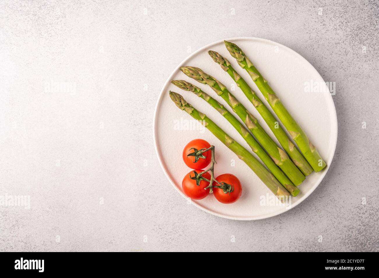 Frischer Spargel und Kirschtomaten auf einem weißen Teller auf hellem Hintergrund mit Kopierraum Draufsicht Stockfoto