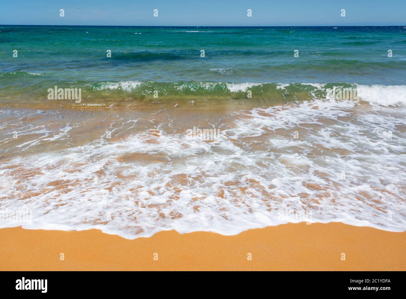 Wellen am Strand mit orange Sand und blauem Wasser Stockfoto